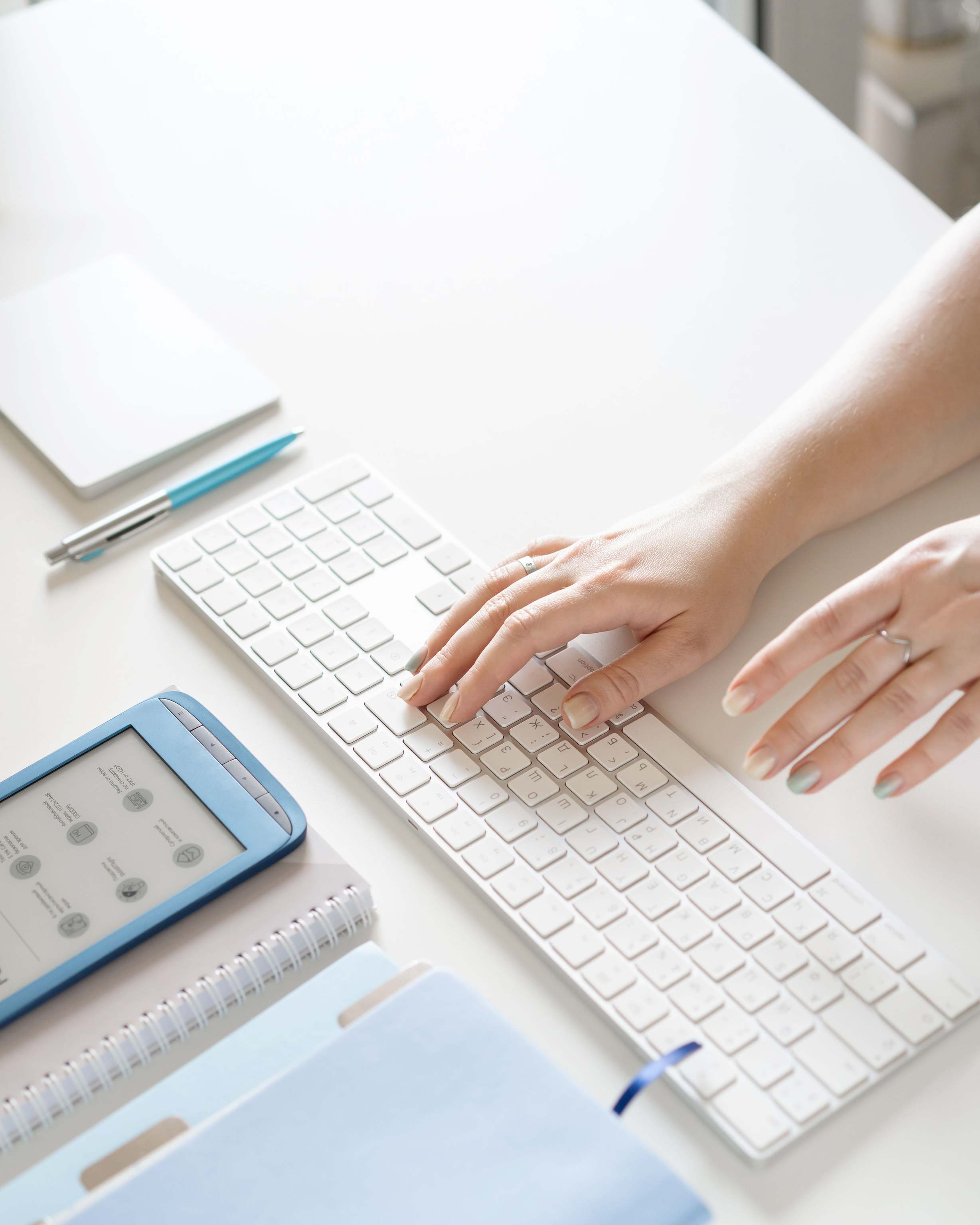 Hands typing on a keyboard beside electronic devices in a modern office